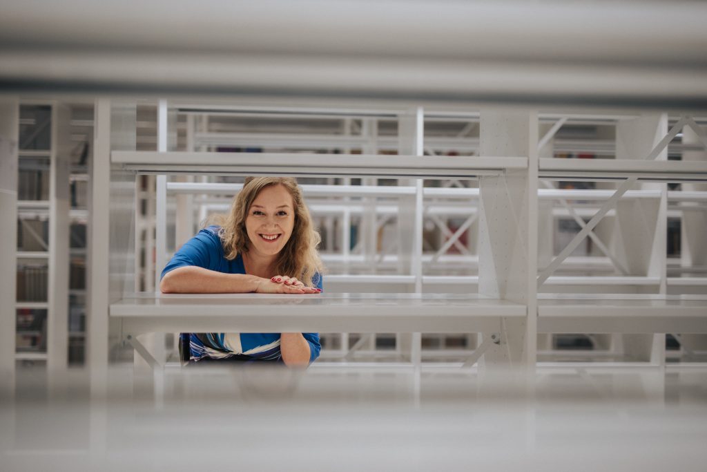 Woman looking through empty book cases, smiling.
