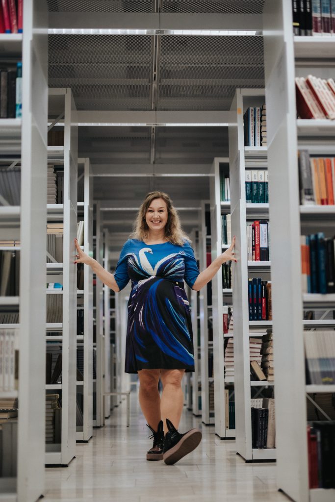 Woman walking between book cases, smiling